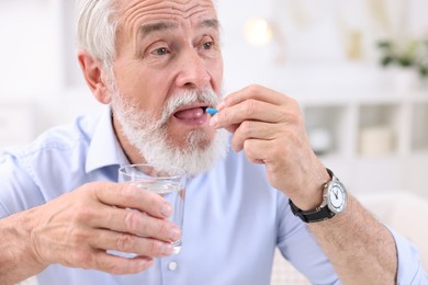 Photo of Senior man with glass of water taking pill at home