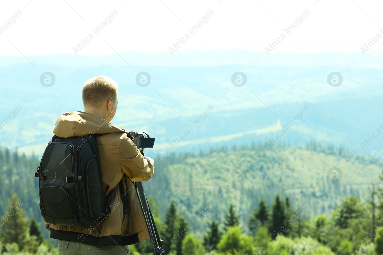 Photo of Photographer with backpack and camera on tripod taking picture of beautiful mountains, back view. Space for text