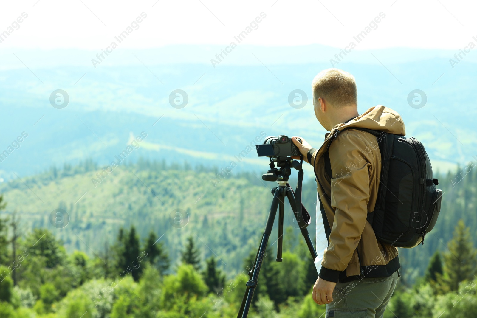 Photo of Photographer with backpack and camera on tripod taking picture of beautiful mountains. Space for text