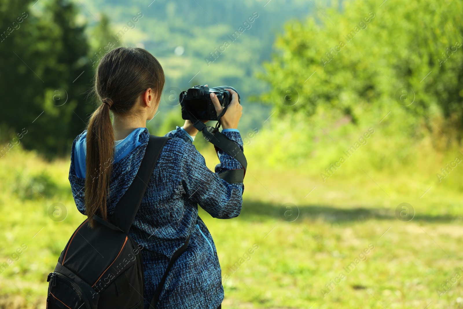 Photo of Photographer with backpack and camera taking picture outdoors, back view. Space for text