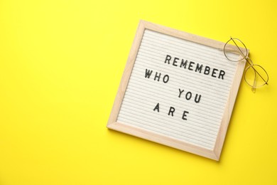 Photo of Letter board with phrase Remember Who You Are and glasses on yellow background, top view. Space for text