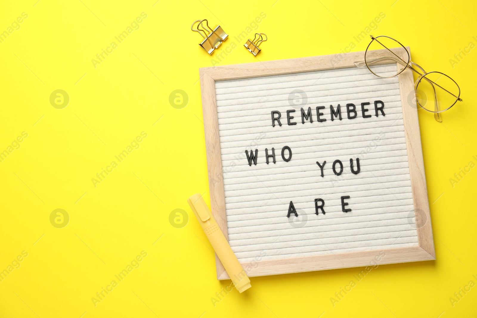 Photo of Letter board with phrase Remember Who You Are, glasses, marker and binder clips on yellow background, flat lay. Space for text