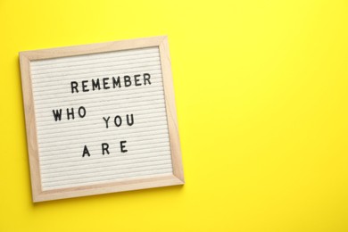 Photo of Letter board with phrase Remember Who You Are on yellow background, top view. Space for text