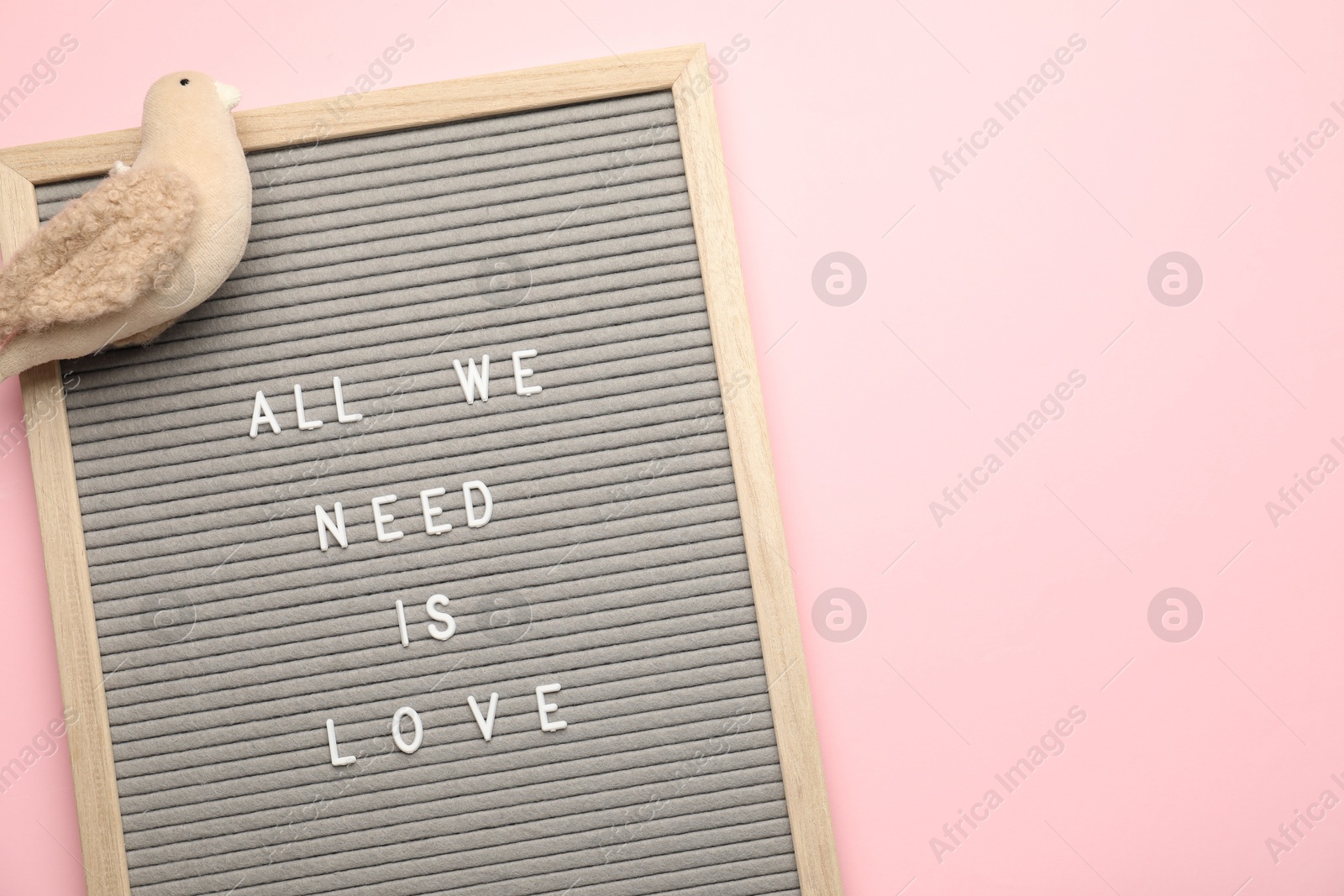 Photo of Letter board with phrase All We Need Is Love and bird figure on pink background, top view. Space for text