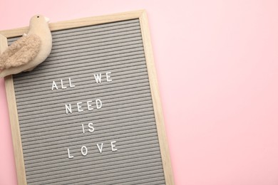 Photo of Letter board with phrase All We Need Is Love and bird figure on pink background, top view. Space for text