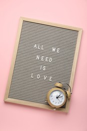 Photo of Letter board with phrase All We Need Is Love and alarm clock on pink background, top view