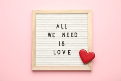 Photo of Letter board with phrase All We Need Is Love and decorative heart on pink background, top view