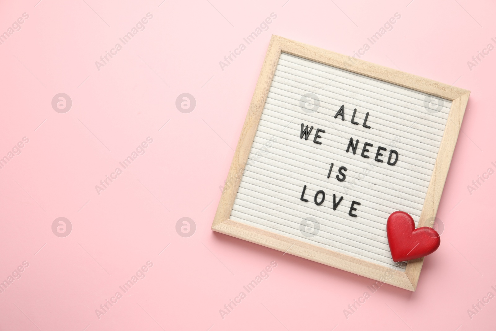 Photo of Letter board with phrase All We Need Is Love and decorative heart on pink background, top view. Space for text