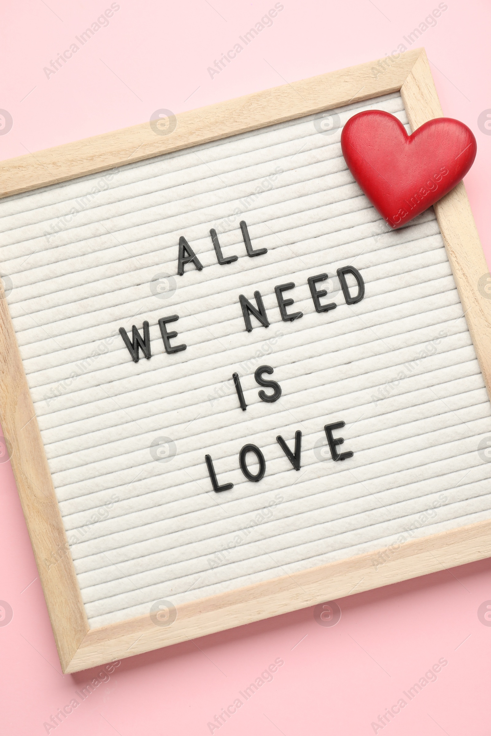 Photo of Letter board with phrase All We Need Is Love and decorative heart on pink background, top view