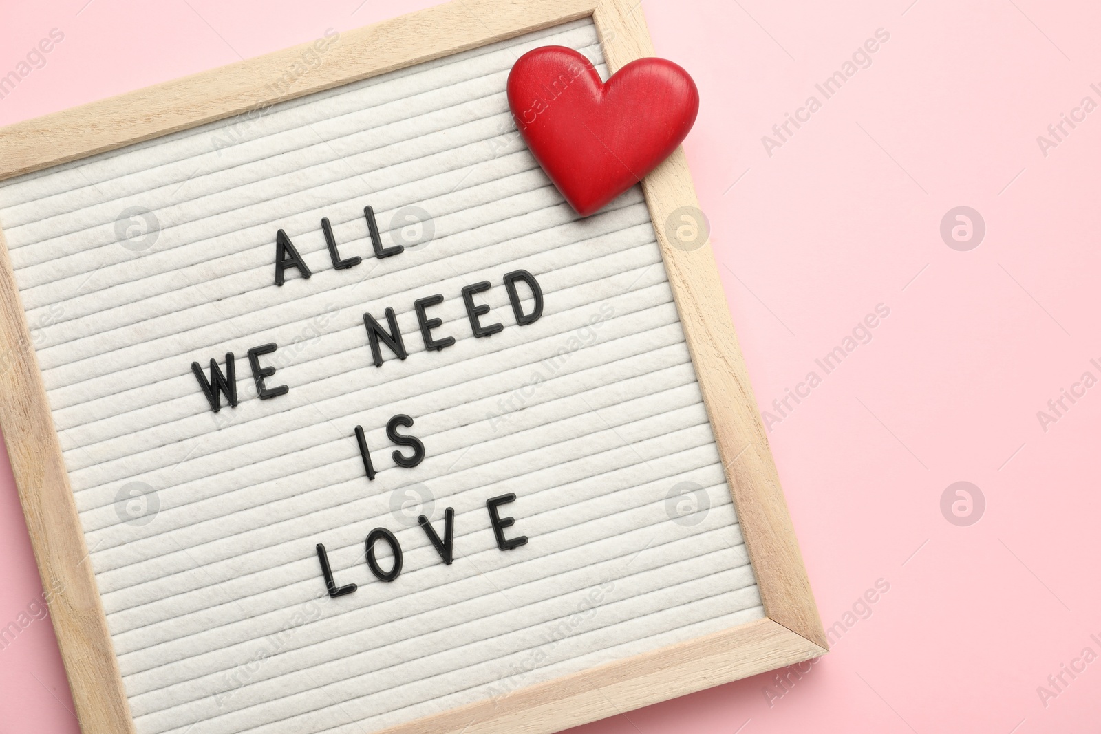 Photo of Letter board with phrase All We Need Is Love and decorative heart on pink background, top view