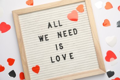 Photo of Letter board with phrase All We Need Is Love and heart shaped confetti on white background, top view