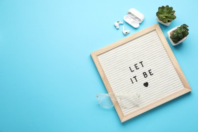 Photo of Letter board with phrase Let It Be, glasses, houseplants and earphones on light blue background, flat lay. Space for text