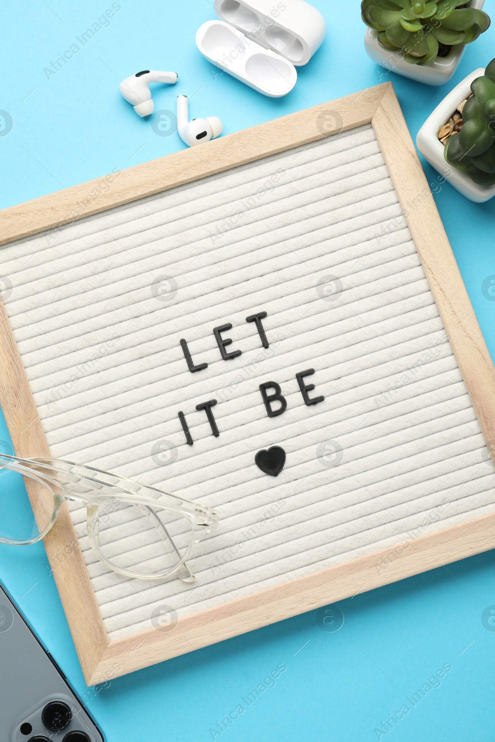 Photo of Letter board with phrase Let It Be, smartphone, glasses, houseplants and earphones on light blue background, flat lay