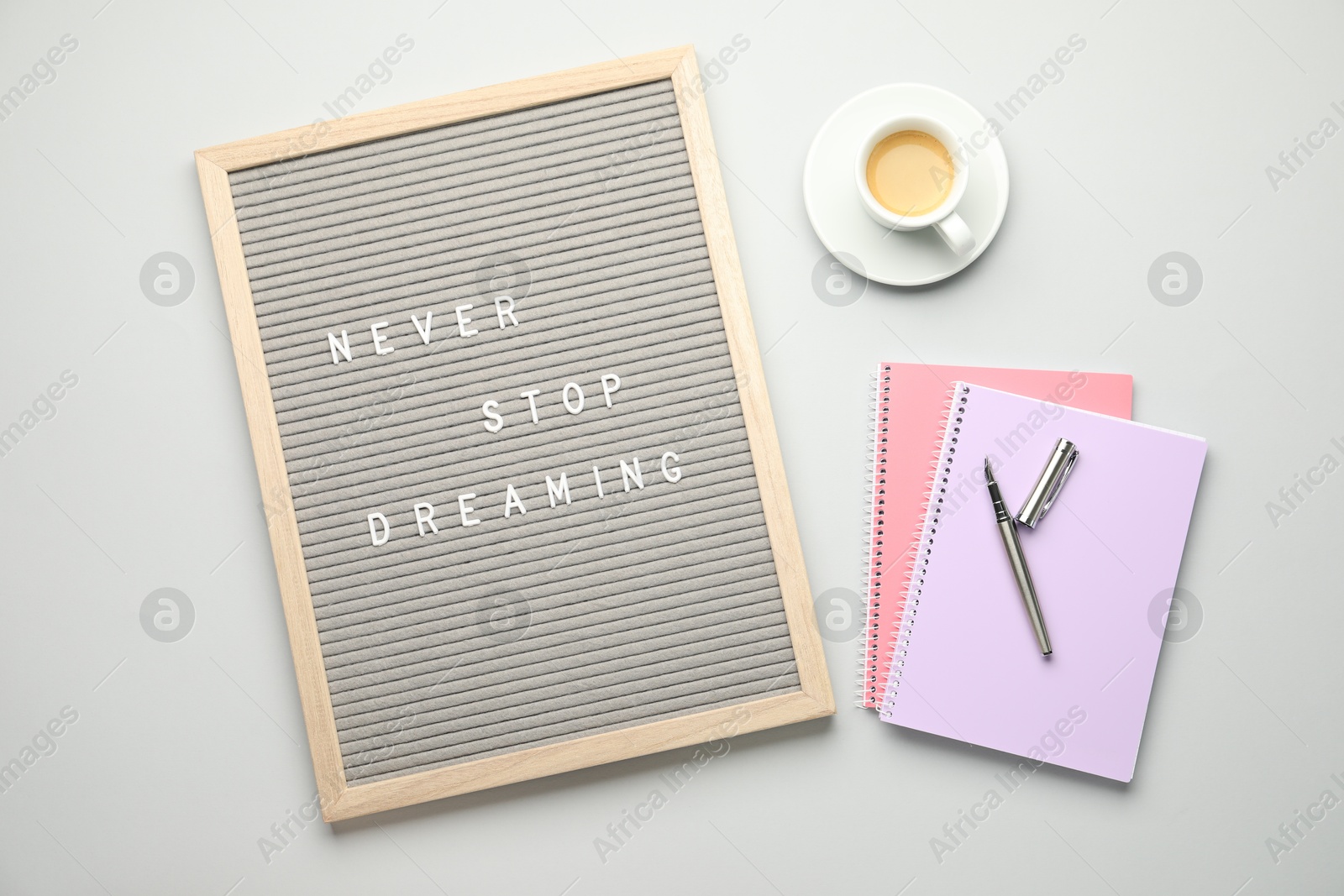 Photo of Letter board with phrase Never Stop Dreaming, notebooks, fountain pen and cup of coffee on light table, flat lay