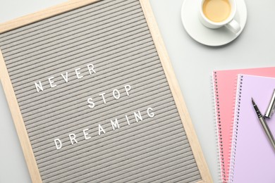 Letter board with phrase Never Stop Dreaming, notebooks, fountain pen and cup of coffee on light table, flat lay