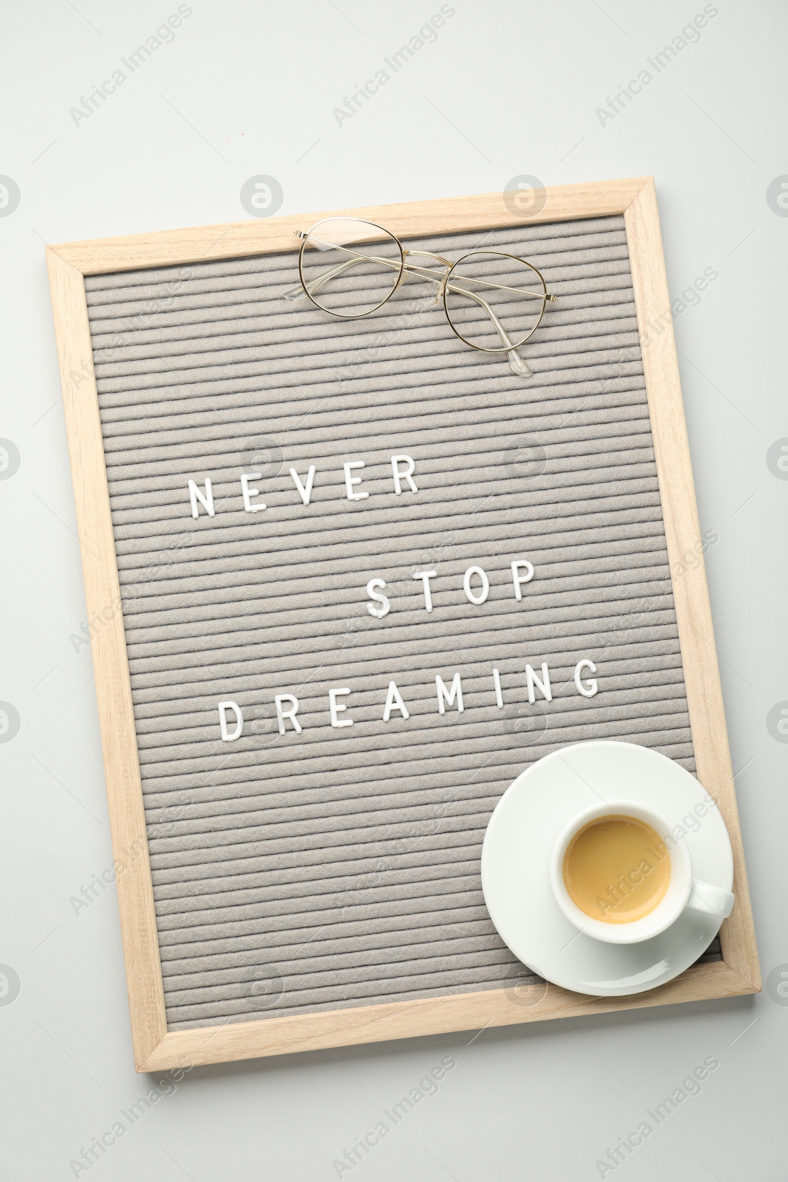 Photo of Letter board with phrase Never Stop Dreaming, glasses and cup of coffee on light table, top view