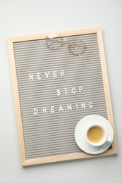 Letter board with phrase Never Stop Dreaming, glasses and cup of coffee on light table, top view