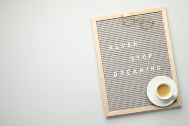 Photo of Letter board with phrase Never Stop Dreaming, glasses and cup of coffee on light table, top view. Space for text