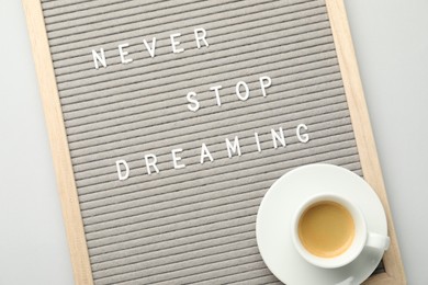 Photo of Letter board with phrase Never Stop Dreaming and cup of coffee on light table, top view