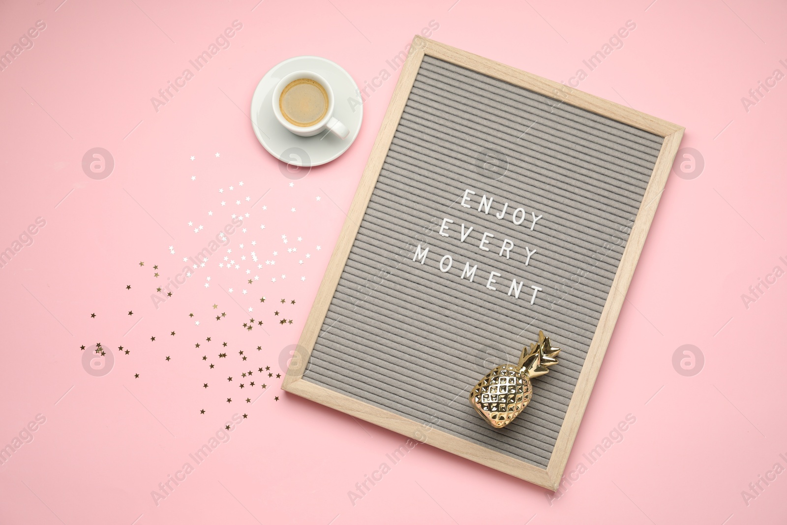 Photo of Letter board with phrase Enjoy Every Moment, cup of coffee, pineapple figure and confetti on pink table, flat lay