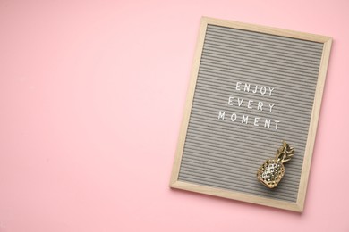 Letter board with phrase Enjoy Every Moment and pineapple figure on pink background, top view. Space for text