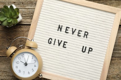 Photo of Letter board with phrase Never Give Up, alarm clock and succulent on wooden table, flat lay