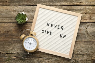 Photo of Letter board with phrase Never Give Up, alarm clock and succulent on wooden table, flat lay