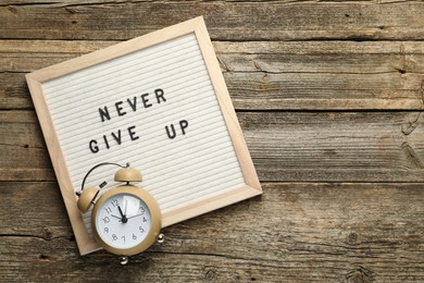 Letter board with phrase Never Give Up and alarm clock on wooden table, top view. Space for text