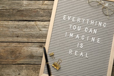 Photo of Letter board with phrase Everything You Can Imagine Is Real, glasses, pen and binder clips on wooden background, top view. Space for text