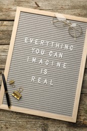 Photo of Letter board with phrase Everything You Can Imagine Is Real, glasses, pen and binder clips on wooden background, top view