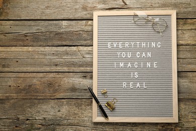 Photo of Letter board with phrase Everything You Can Imagine Is Real, glasses, pen and binder clips on wooden background, top view. Space for text