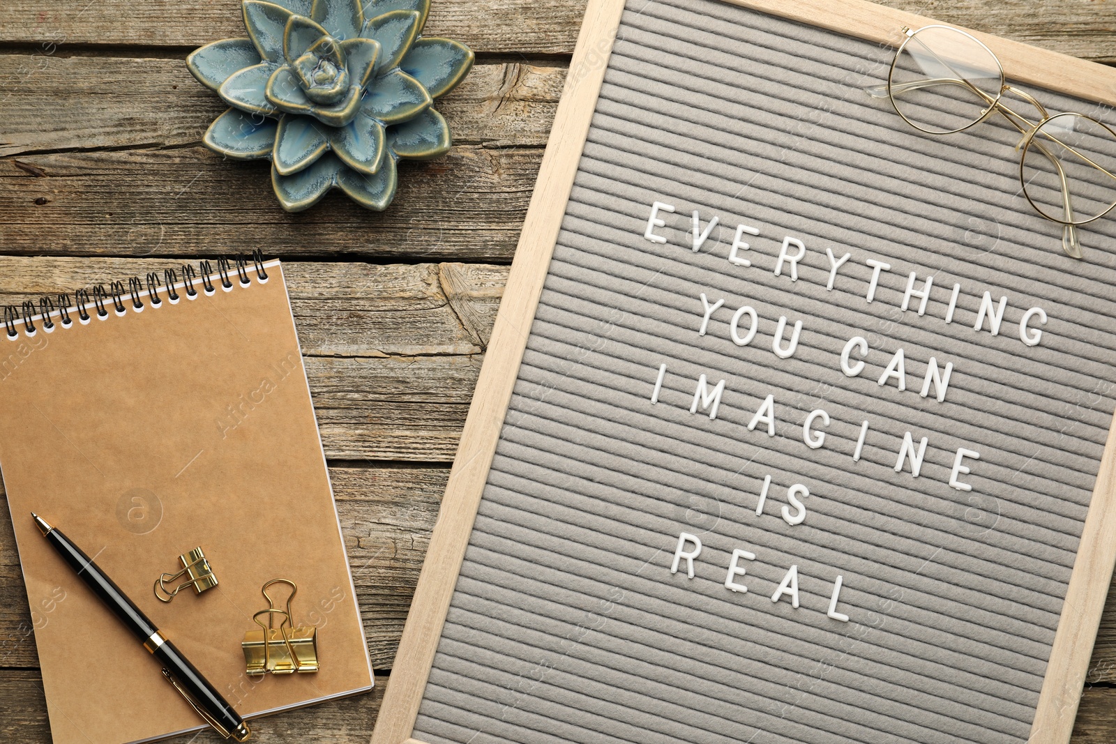 Photo of Letter board with phrase Everything You Can Imagine Is Real, stationery, glasses, succulent, pen and binder clips on wooden background, flat lay