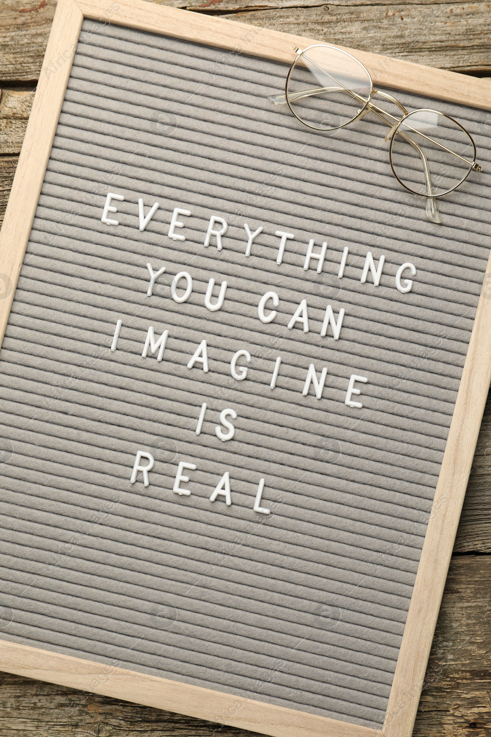 Photo of Letter board with phrase Everything You Can Imagine Is Real and glasses on wooden background, top view