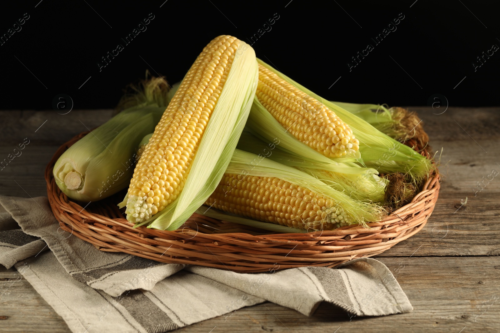 Photo of Many fresh ripe corncobs with green husks on wooden table