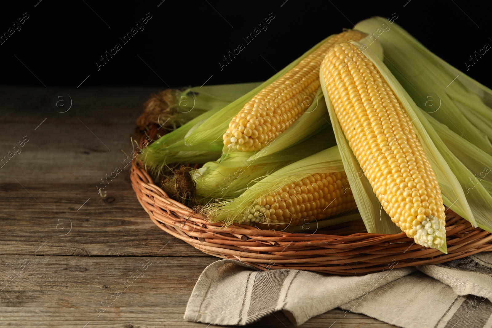 Photo of Many fresh ripe corncobs with green husks on wooden table. Space for text