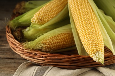 Photo of Many fresh ripe corncobs with green husks on wooden table, closeup