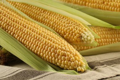 Many fresh ripe corncobs with green husks on table, closeup