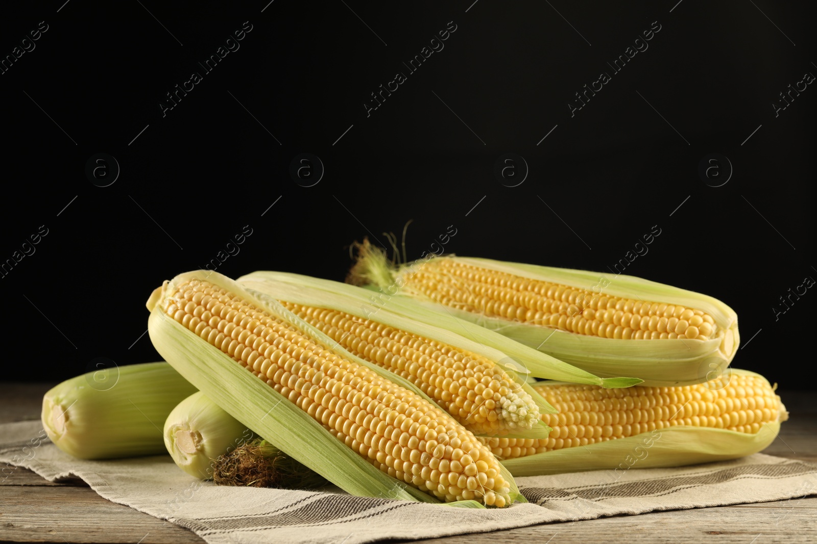 Photo of Many fresh ripe corncobs with green husks on wooden table. Space for text