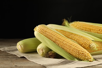 Many fresh ripe corncobs with green husks on wooden table