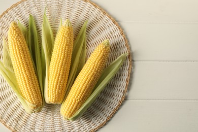 Photo of Many fresh ripe corncobs with green husks on white wooden table, top view. Space for text