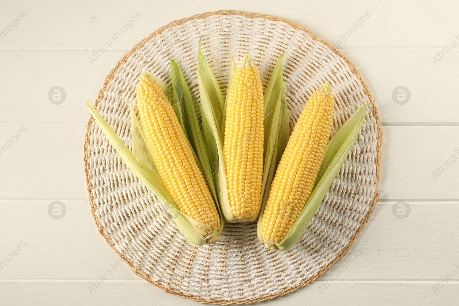 Photo of Many fresh ripe corncobs with green husks on white wooden table, top view