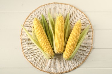 Many fresh ripe corncobs with green husks on white wooden table, top view