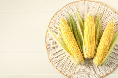 Photo of Many fresh ripe corncobs with green husks on white wooden table, top view. Space for text