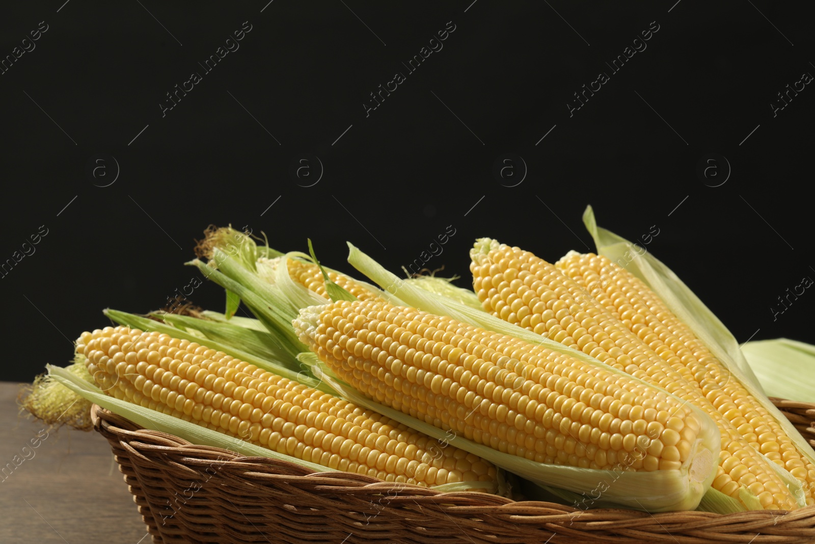 Photo of Many fresh ripe corncobs with green husks on wooden table