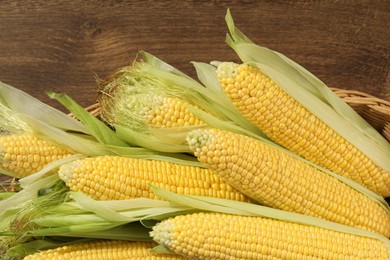 Photo of Many fresh ripe corncobs with green husks on wooden , closeup