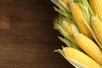 Photo of Many fresh ripe corncobs with green husks on wooden table, top view. Space for text