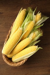 Photo of Many fresh ripe corncobs with green husks on wooden table, top view