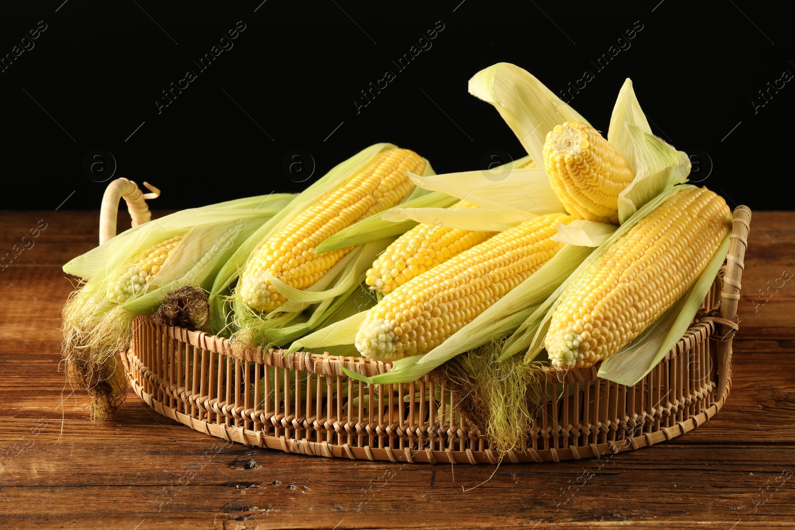 Photo of Many fresh ripe corncobs with green husks on wooden table