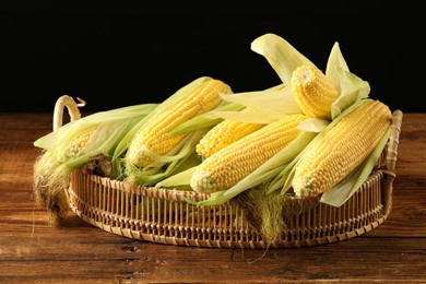 Photo of Many fresh ripe corncobs with green husks on wooden table