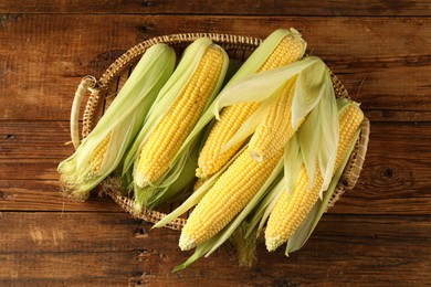 Photo of Many fresh ripe corncobs with green husks on wooden table, top view